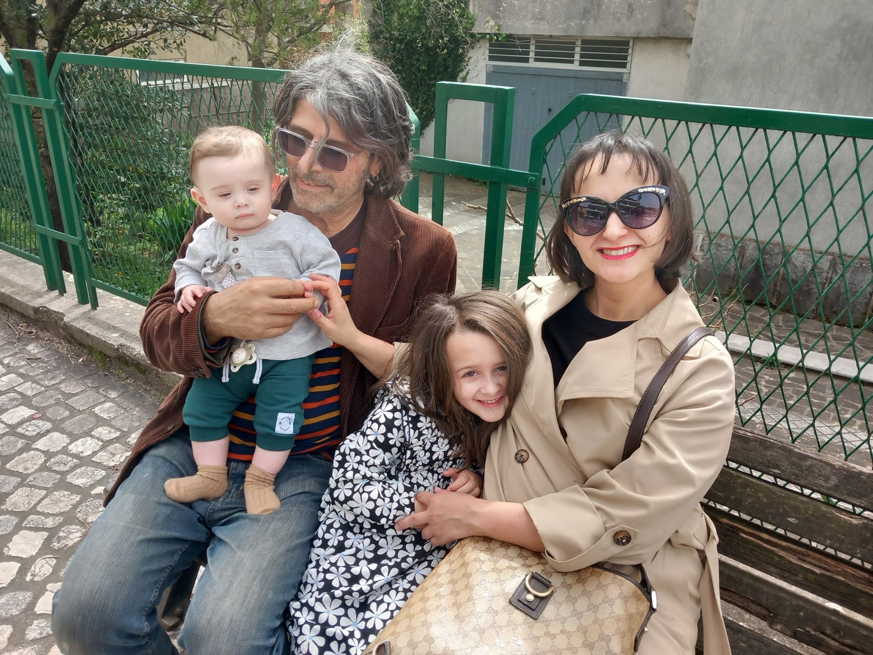 A woman with her husband and two young kids sitting outside on a bench.