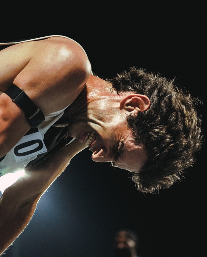 photo of man exhausted after nighttime race, bending over with head down