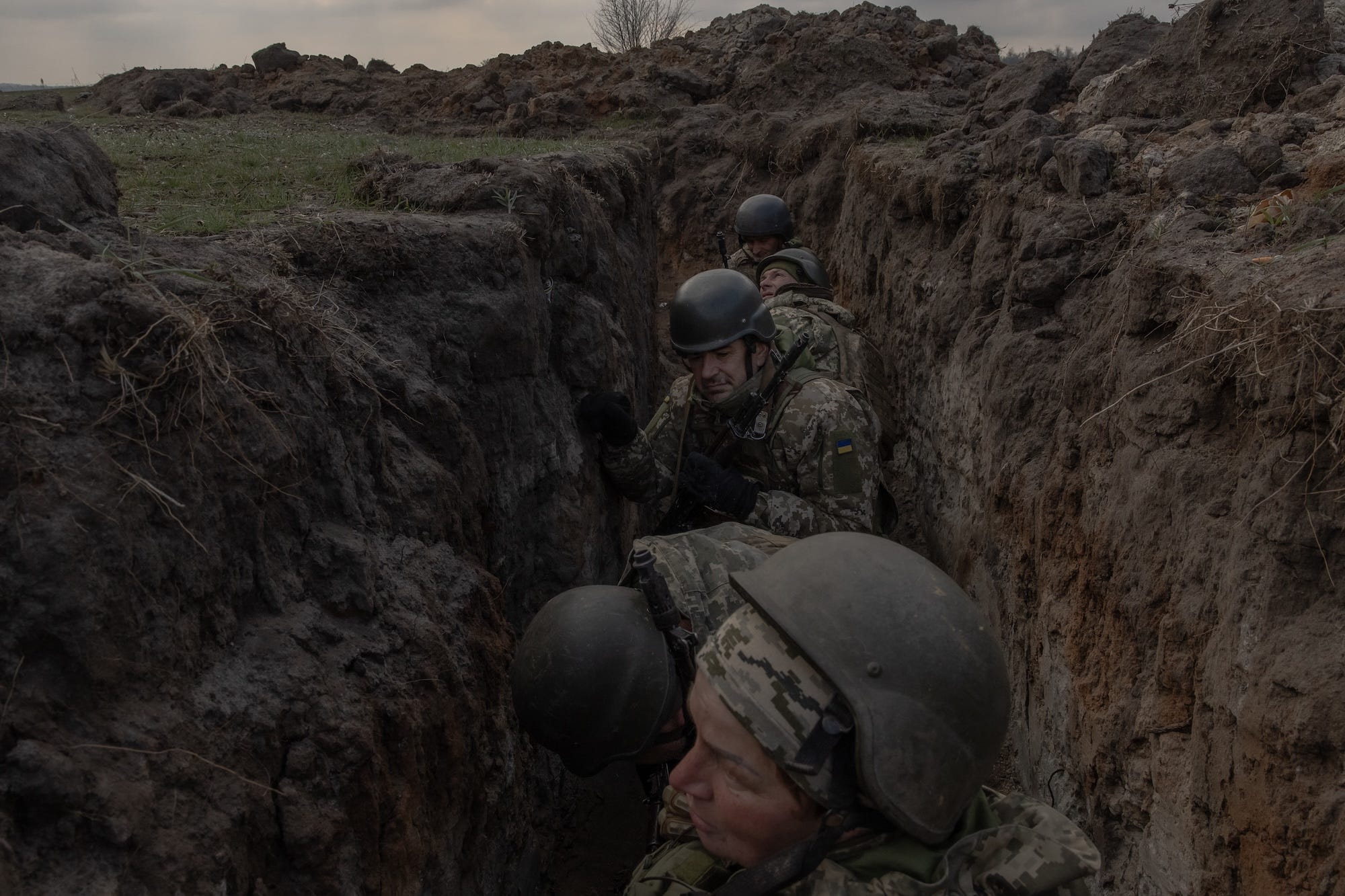 A row of figures in camouflage gear and helmets in a muddy trench