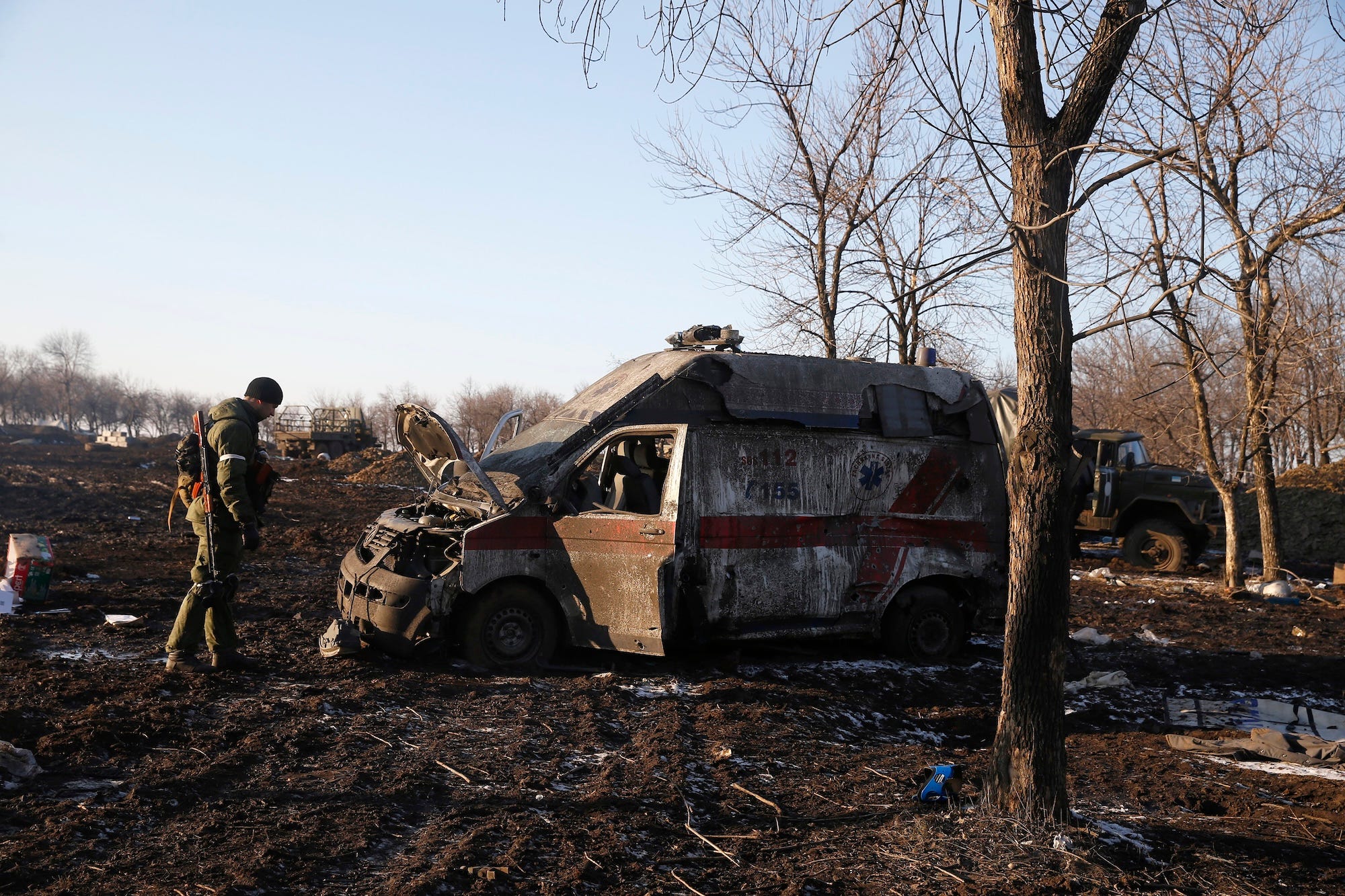 A destroyed white and red vehicle in a field with a man looking on