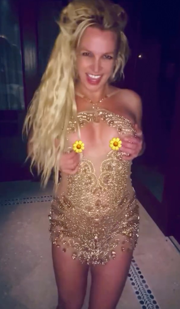 Britney Spears in a sparkly gold minidress with flower emojis covering her breasts.