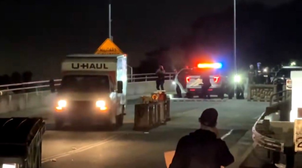 A U-Haul truck drives towards an illuminated police vehicle and officers at night.