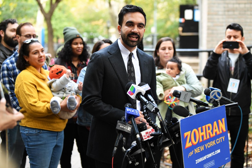 NYC mayoral candidate Zohran Mamdani speaking at a press conference with babies and new parents around him.