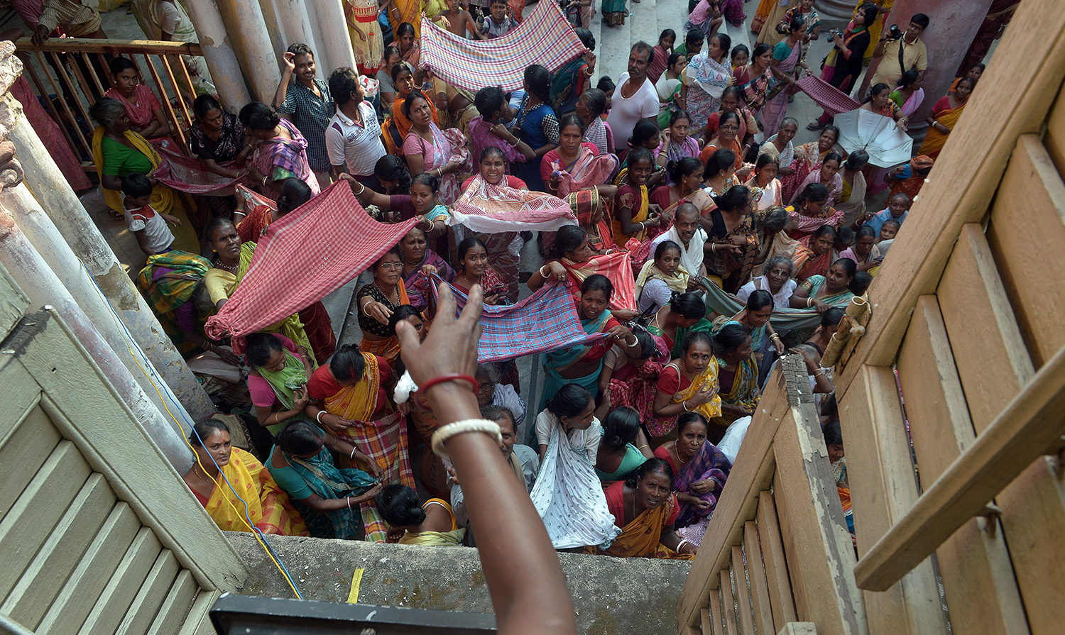 A hand reaches out of an open window tossing rice to a large crowd below that's holding up clothes to catch it.
