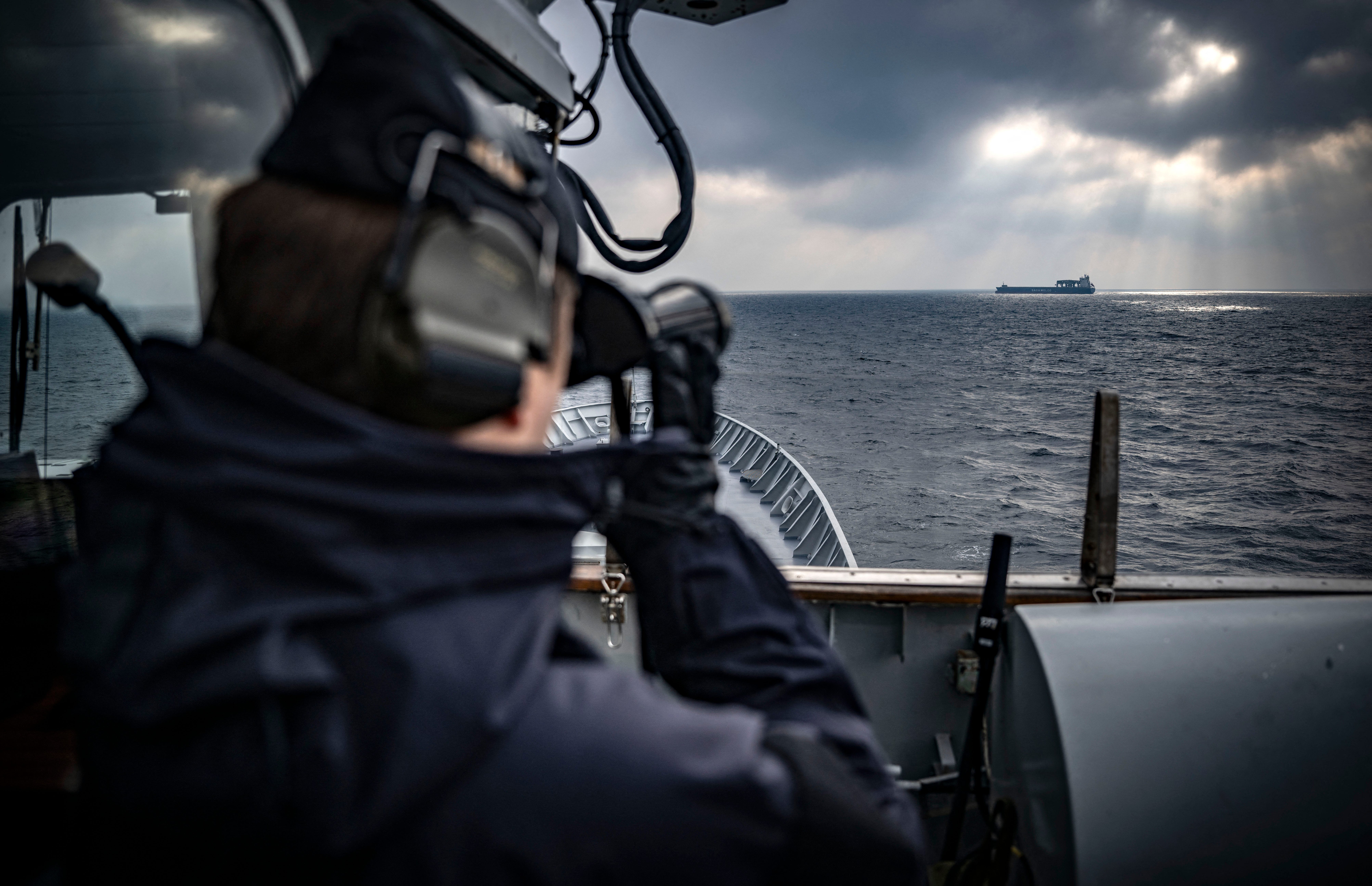 A picture taken on February 4, 2025, shows a cargo ship on the horizon as a crew member is on lookout with binoculars from the bridge deck of patrol ship HMS Carlskrona (P04), on open water near Karlskrona, Sweden, as part of the NATO Baltic Sea patrol mission, the Baltic Sentry, aimed to secure critical underwater infrastructure.