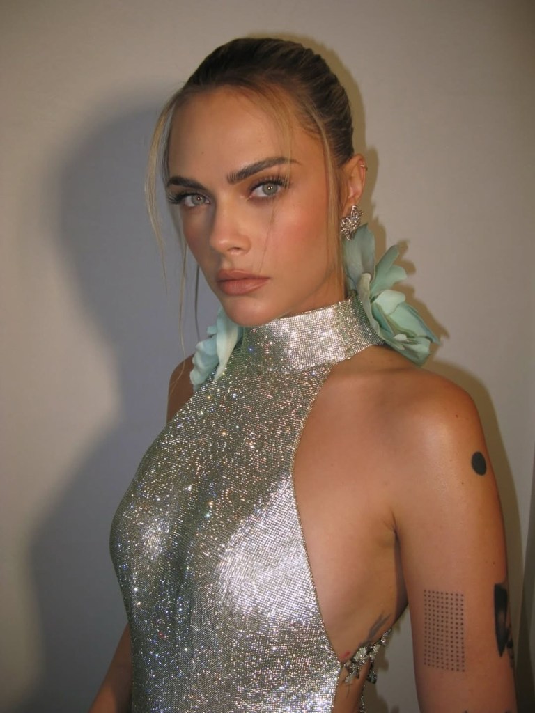 Cara Delevingne in a sparkling silver halter top with light blue fabric flowers on the shoulders.