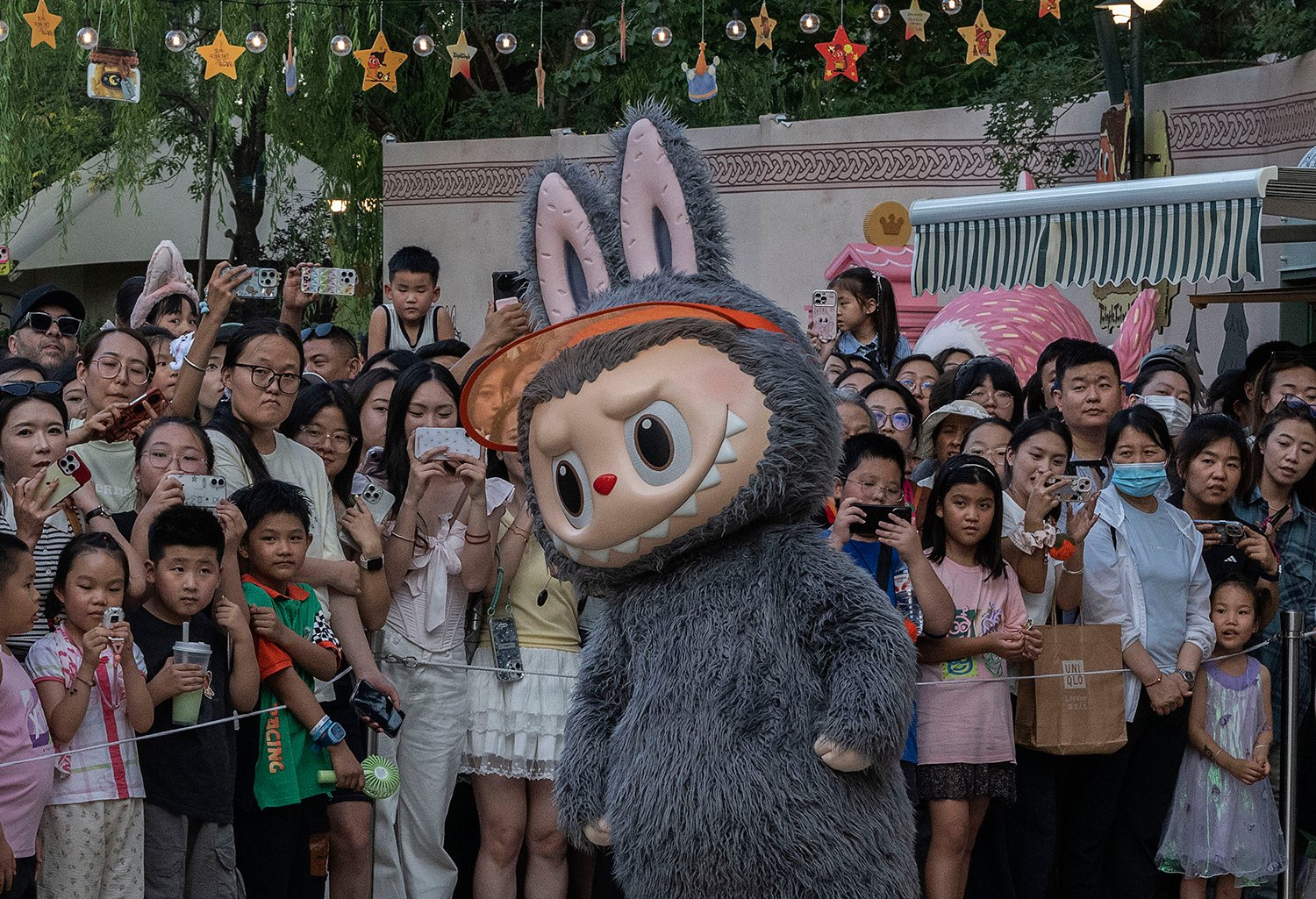 A performer in a Labubu costume dances, surrounded by a large crowd of people.