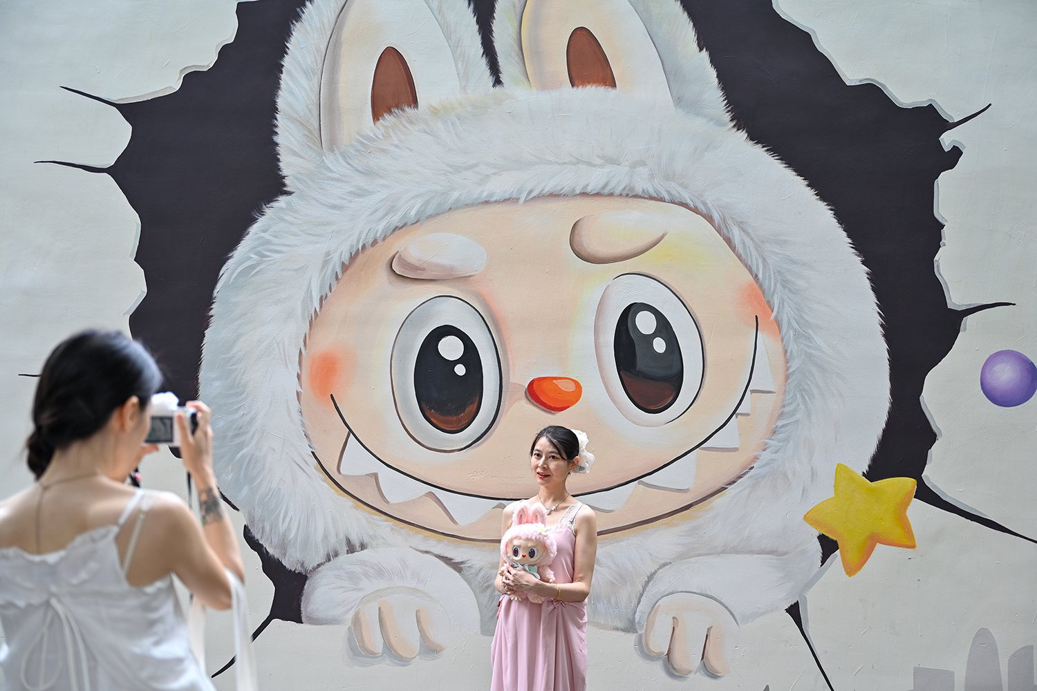 A visitor poses for a photo with Labubu graffiti