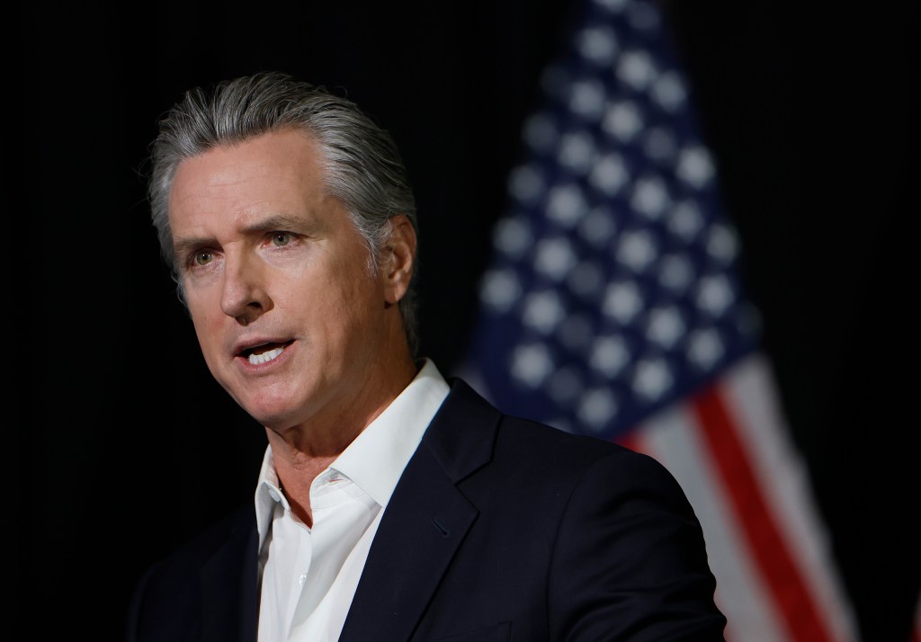 California Gov. Gavin Newsom speaking to reporters with an American flag in the background.