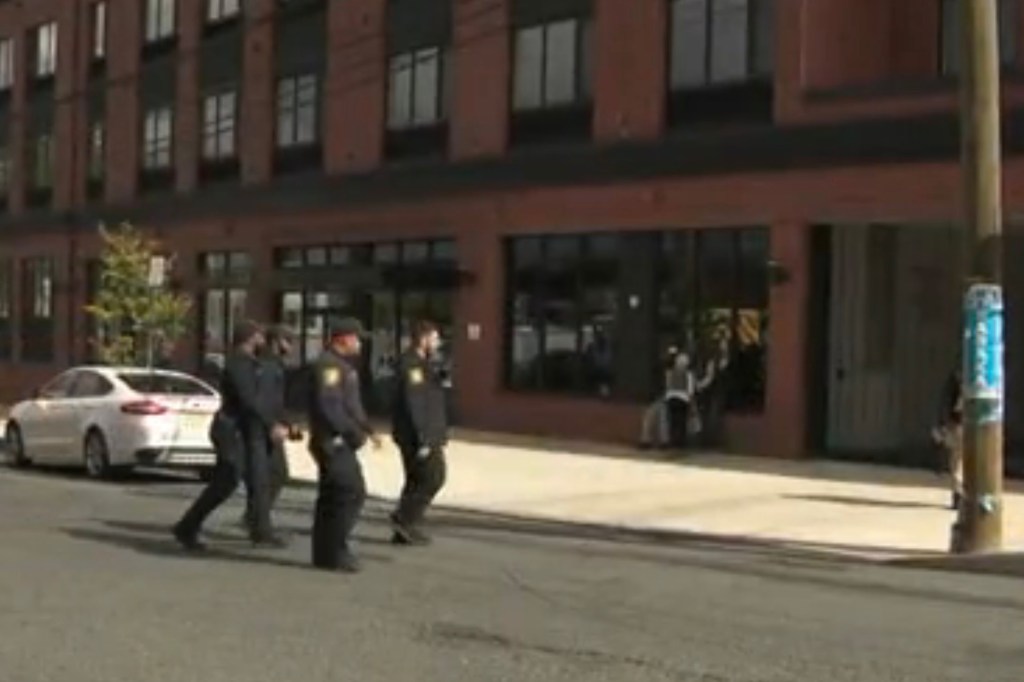 Three police officers walk along a street in front of a brick building.