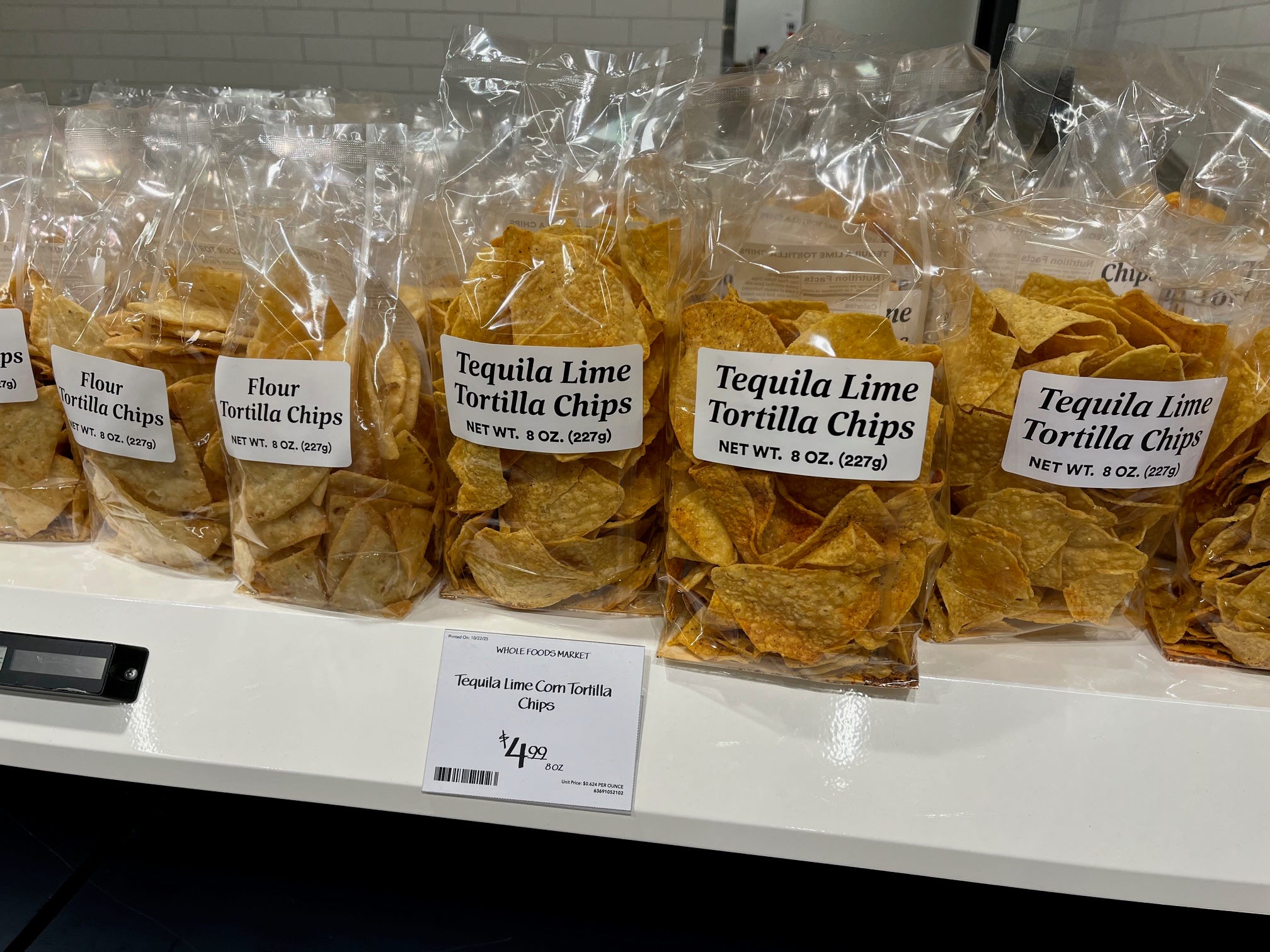 Transparent plastic bags of Tequila Lime Tortilla Chips sit on a shelf at Whole Foods Daily Shop.