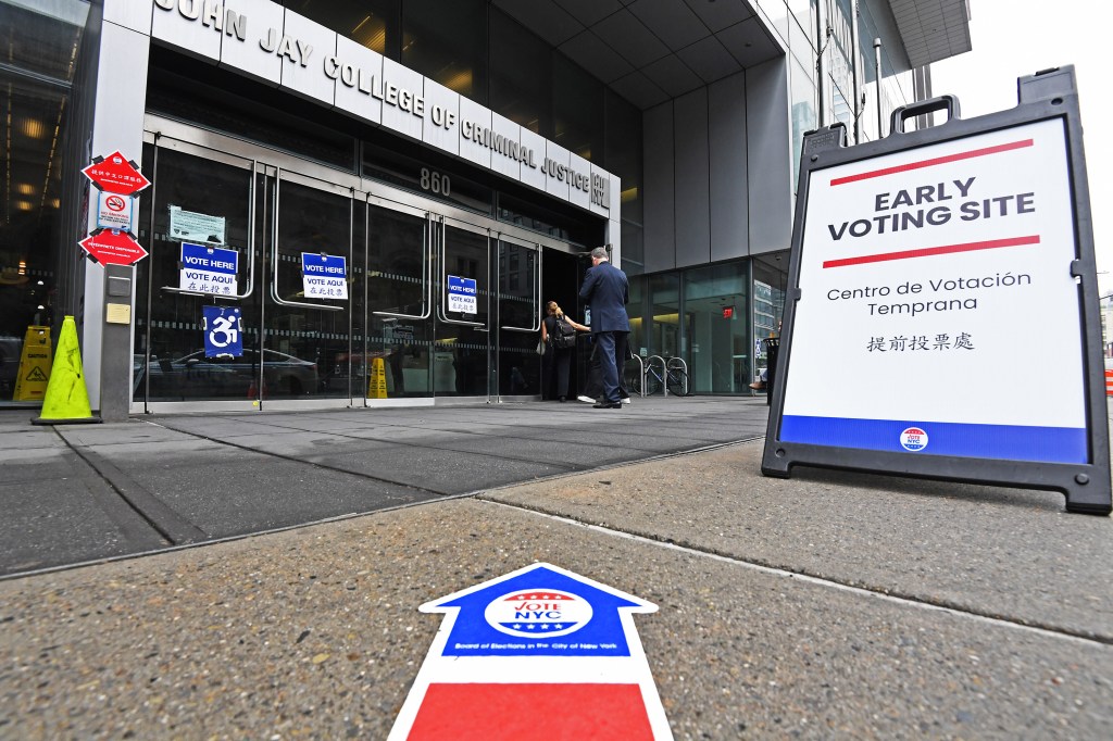 People entering the John Jay College of Criminal Justice building, designated as an early voting site in NYC, with voting signs on the pavement and door.