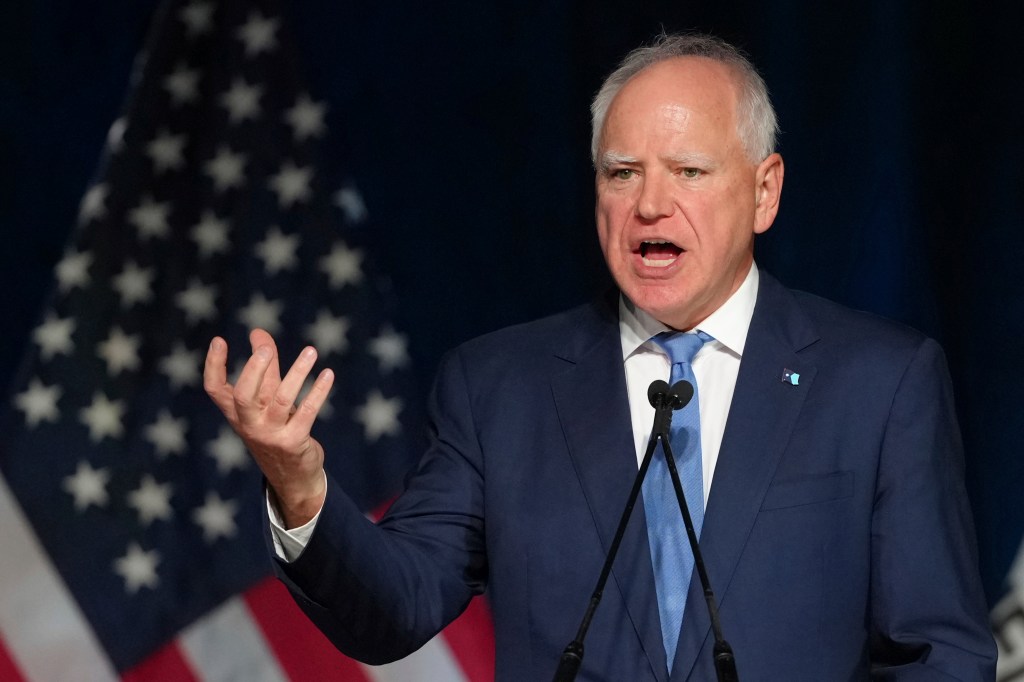 Minnesota Gov. Tim Walz speaking at an event, with an American flag visible in the background.
