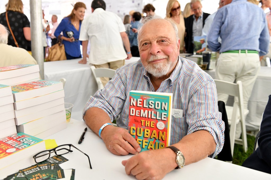 demille sits at a table with a copy of his book the cuban affair smiling at the camer