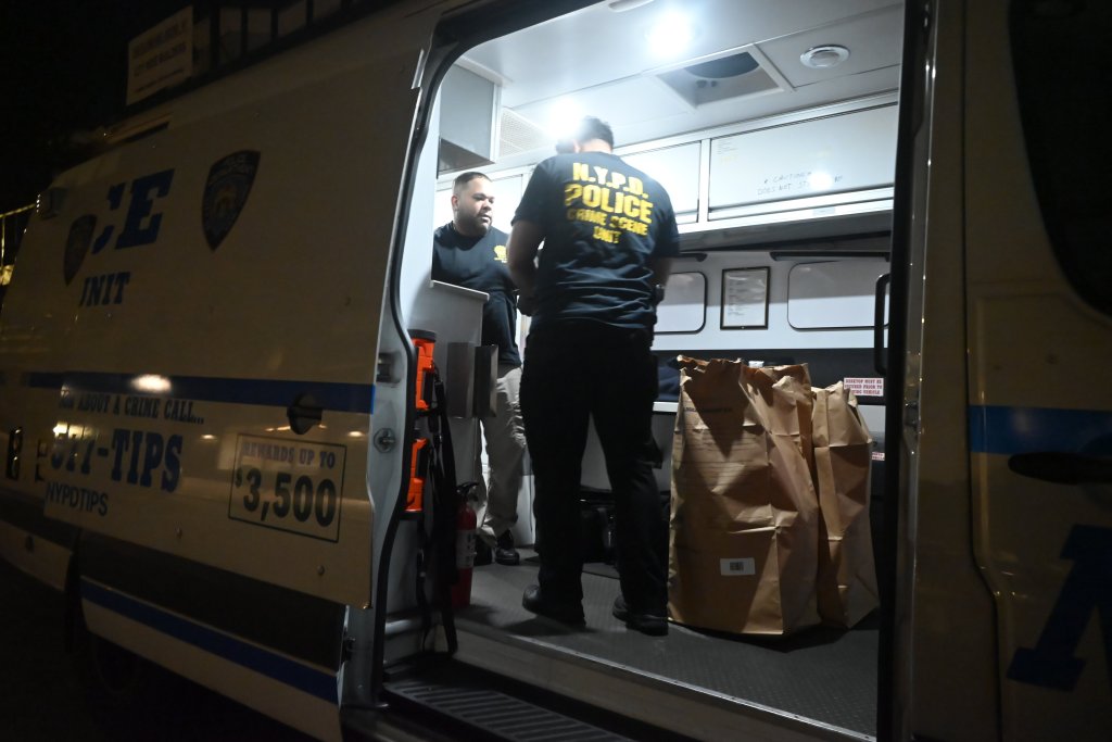 NYPD Crime Scene Unit officers and evidence bags inside a police vehicle at night.