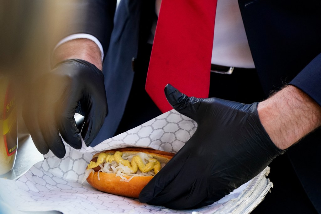 A close-up shot of furloughed federal worker Issac Stein, 31, wearing black gloves as he serves a hot dog with mustard and sauerkraut.