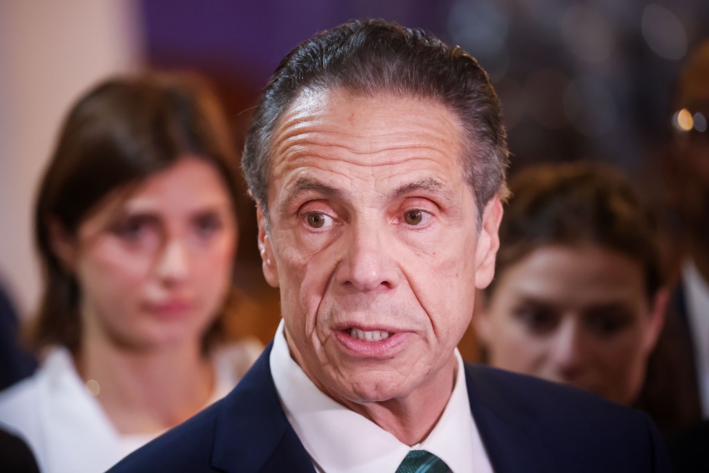Andrew Cuomo speaking at a campaign event, with Michaela Kennedy-Cuomo and Cara Kennedy-Cuomo visible in the background.