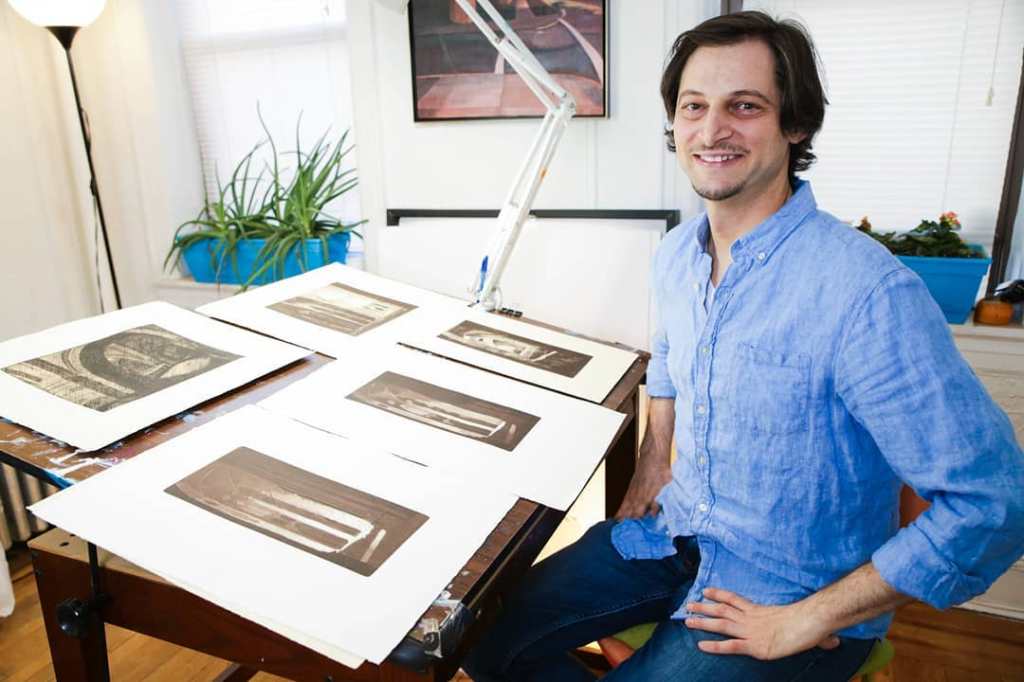 Artist James Haggerty sits at a drafting table with his artwork.