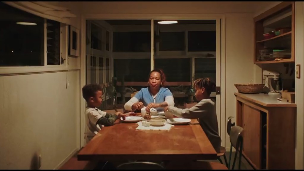 A woman and two young boys sitting around a dining table, setting the table.