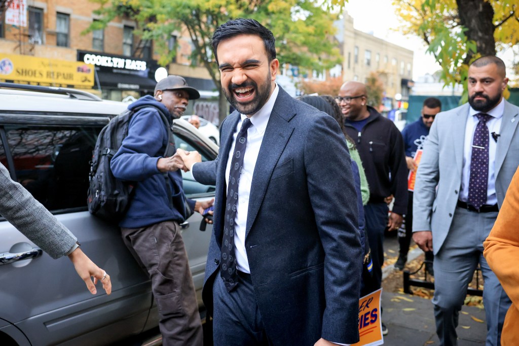 Zohran Mamdani laughing while shaking hands with a man in Flatbush, Brooklyn.
