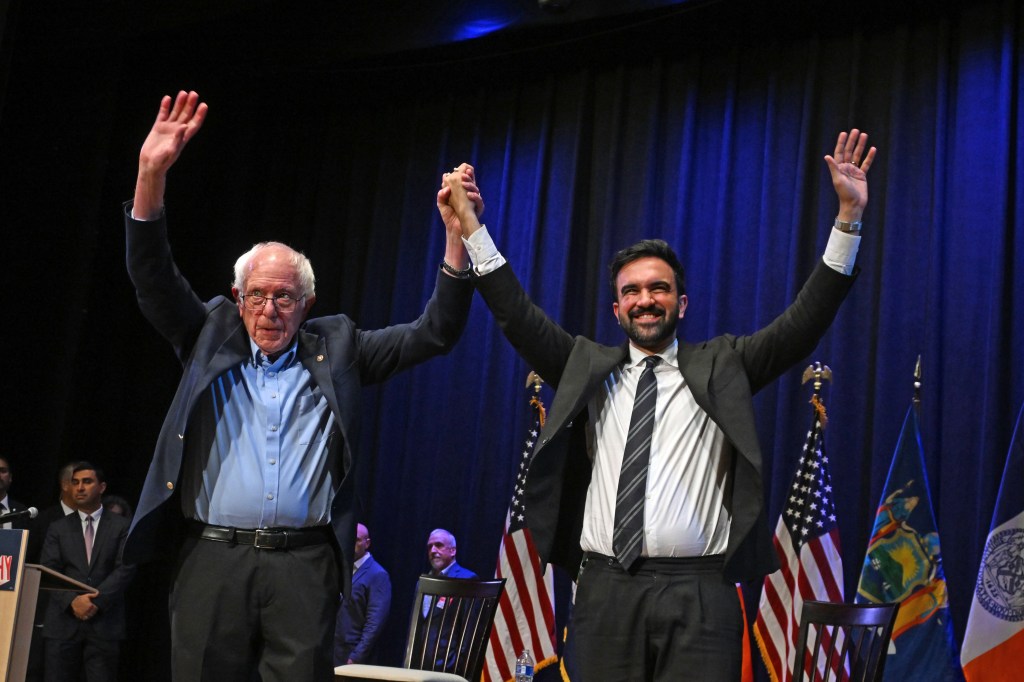 Senator Bernie Sanders and Democratic NYC mayoral candidate Zohran Mamdani raise their hands together at a town hall event.