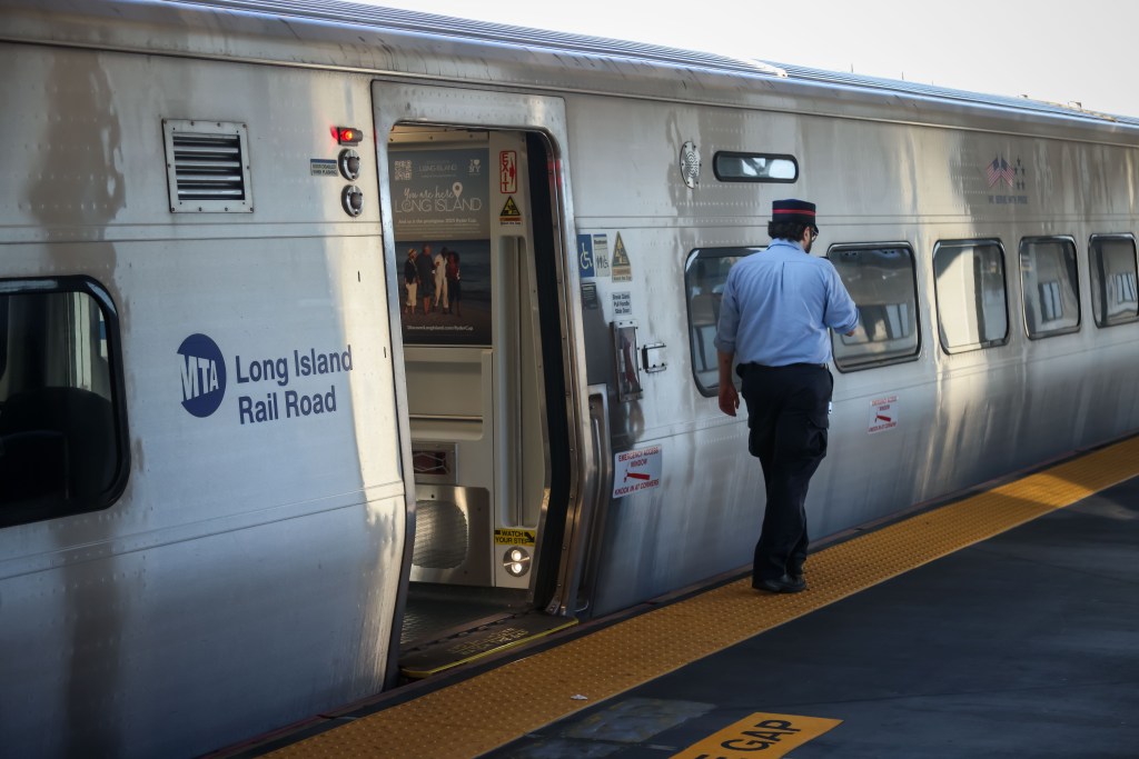 An LIRR employee stands on the platform of the Long Island Rail Road (LIRR) Jamaica Station with a train door open.
