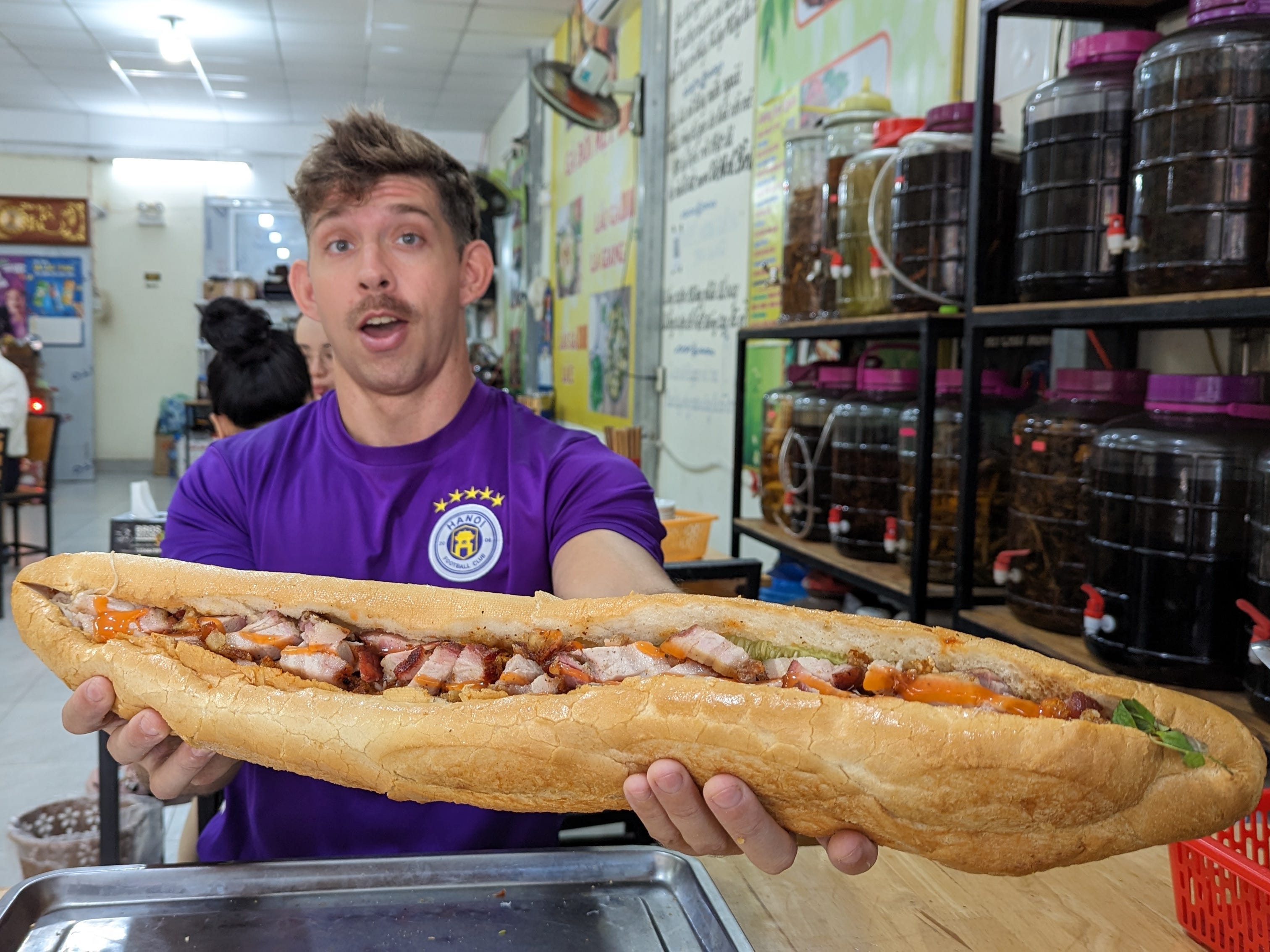 A man holding up a banh mi sandwich in Vietnam.