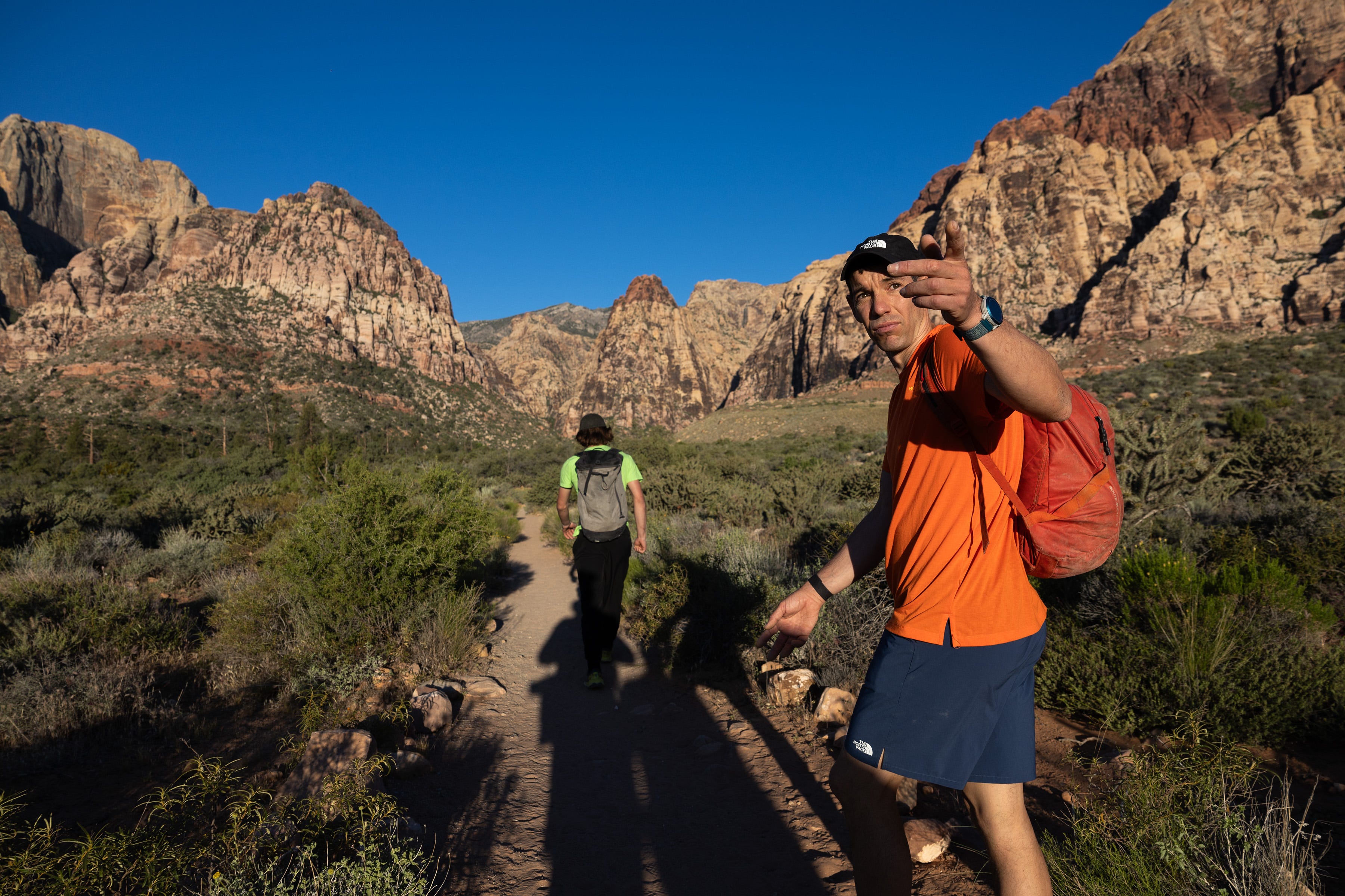 Alex Honnold and a partner hiking through a red canyon.