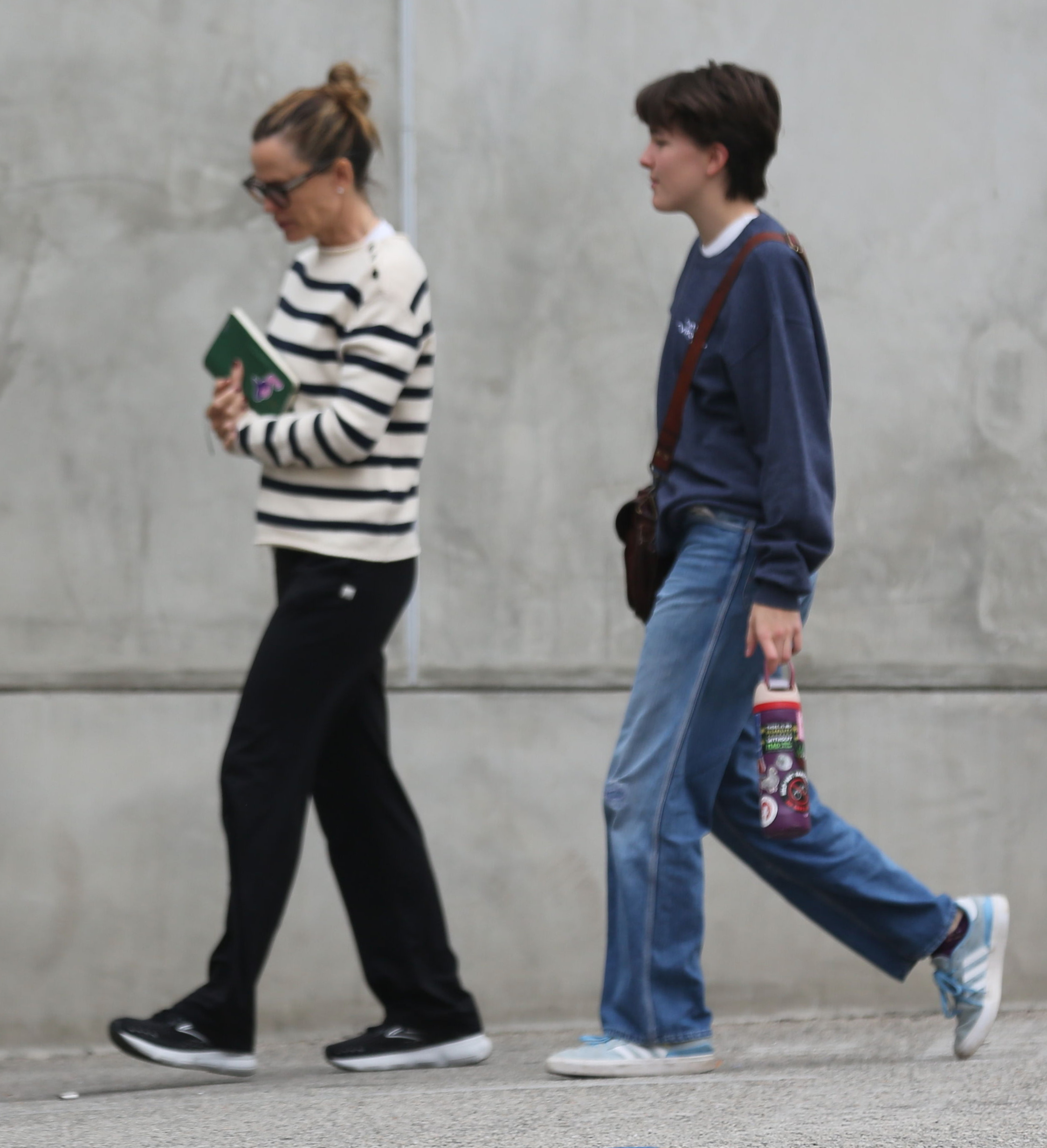 Jennifer Garner in a striped shirt and dark pants walking next to her child, Seraphina, in a navy sweatshirt and baggy jeans.