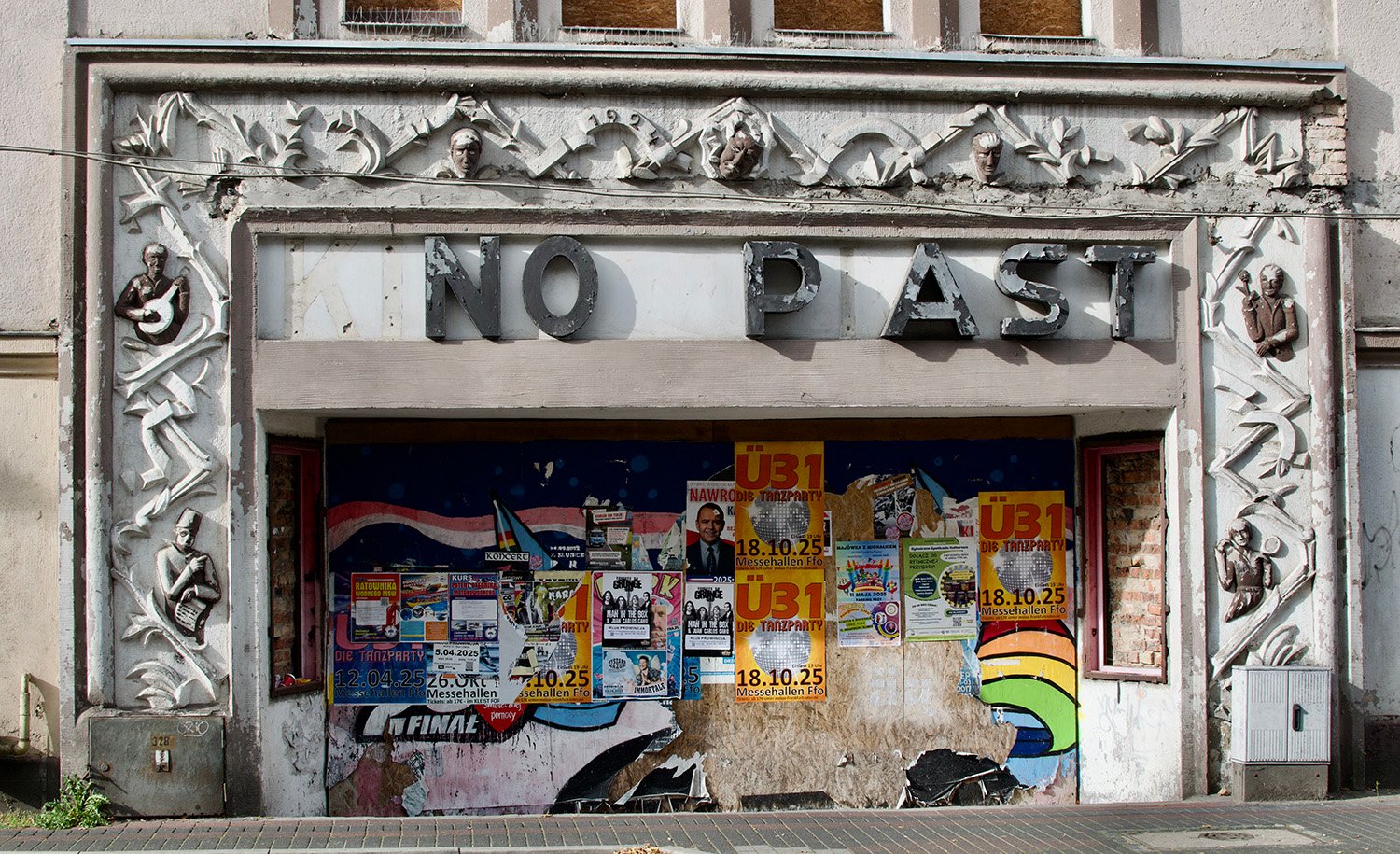 An old movie theater sign with missing letters so that it reads NO P AST. The edifice is covered with posters.