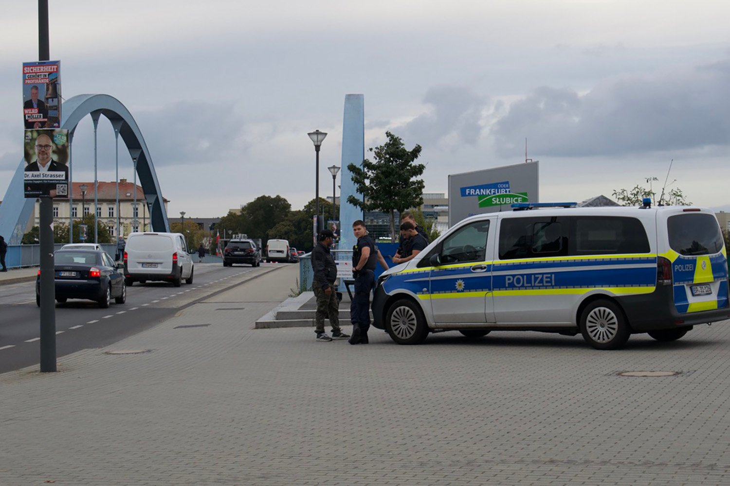 Police offers stand next to a van at the entrance to a bridge.