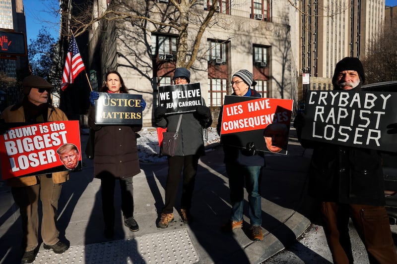 NEW YORK, NEW YORK - JANUARY 22: Protestors hold up signs outside of Manhattan Federal Court before the start of the E. Jean Carroll civil defamation trial against former President Donald Trump on January 22, 2024 in New York City. Former President Trump is scheduled to testify in his civil defamation trial on the eve of the New Hampshire primary. A verdict is expected this week in the trial that will decide how much money in damages the former president will have to pay Carroll for his 2019 defamatory statements about her sexual assault allegations.   (Photo by Michael M. Santiago/Getty Images)