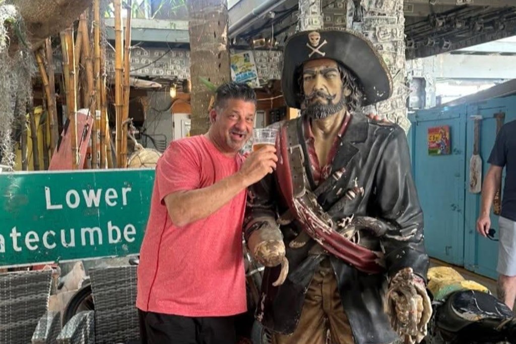 Mark Calcagni holding a glass of beer next to a pirate statue.