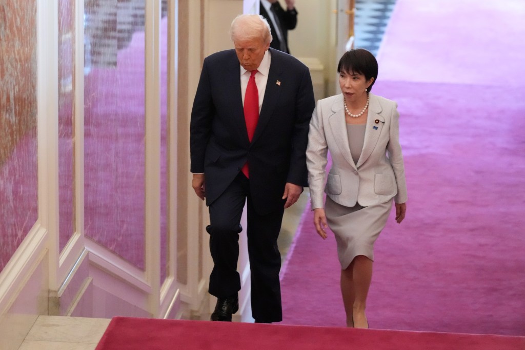 Donald Trump and Sanae Takaichi walking down a staircase with a red carpet.
