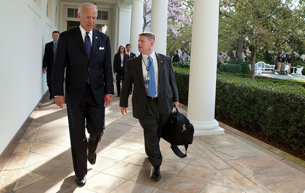Joe Biden walks alongside his physician, Kevin O'Connor, on a paved outdoor pathway.