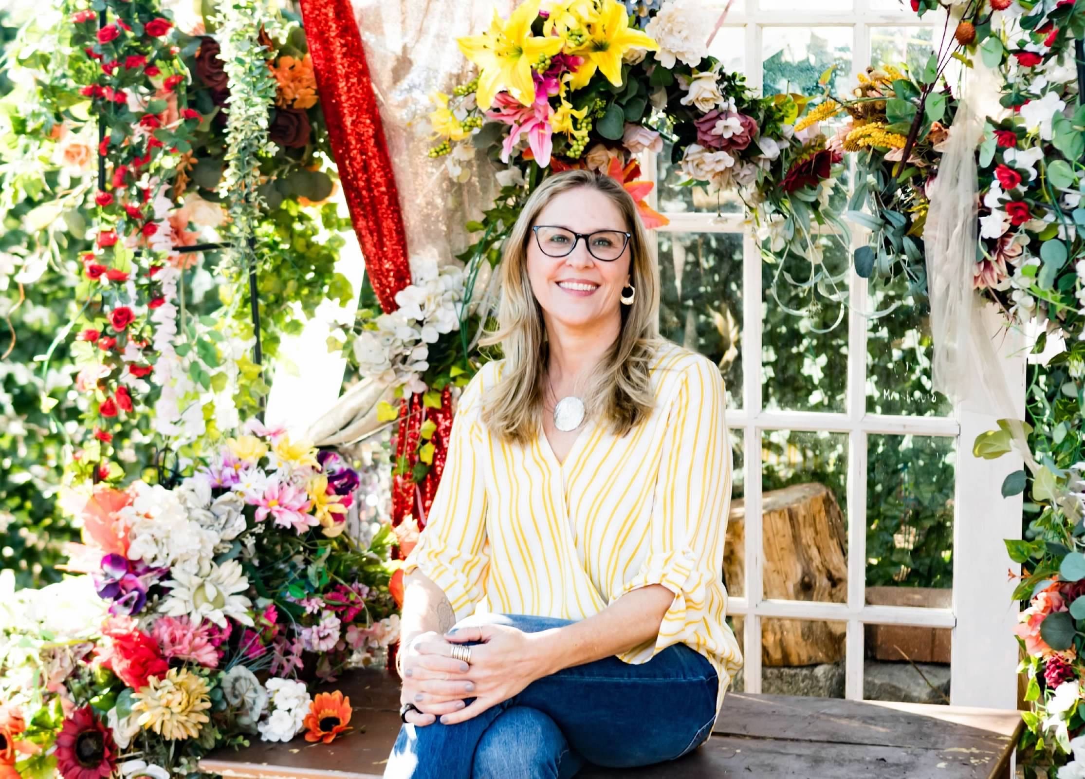 Author Heather Sweeney poses among flowers and other plants.