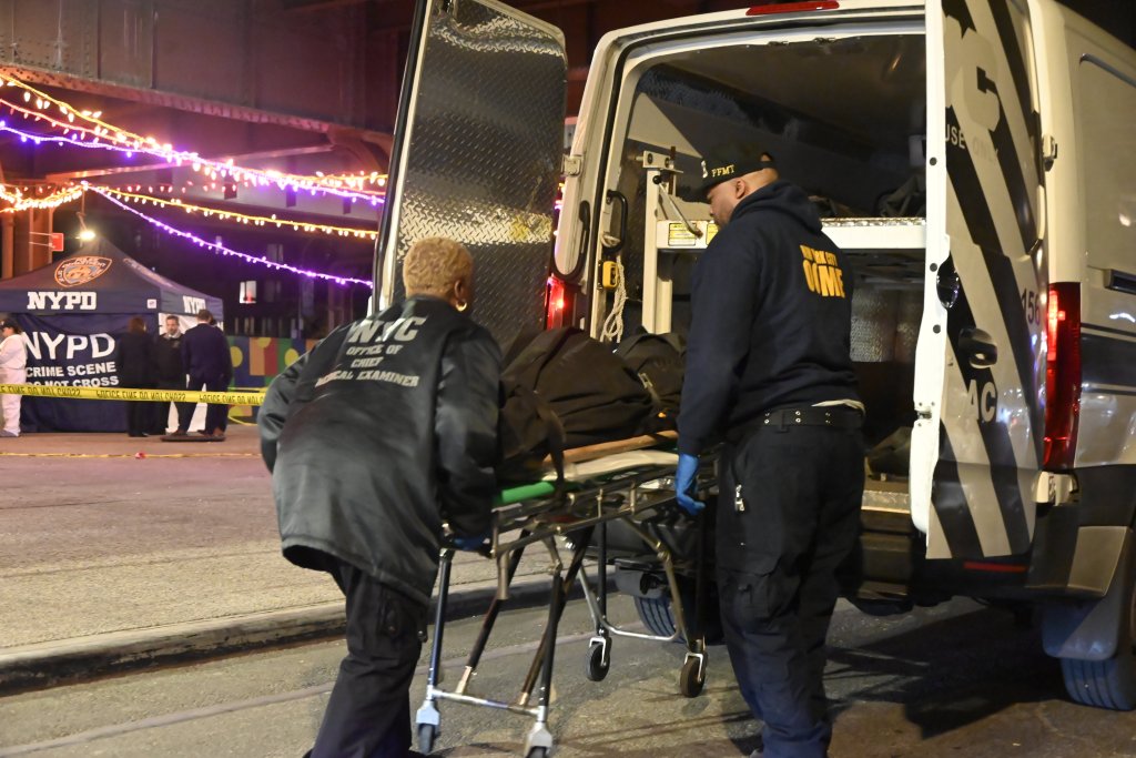 Medical examiners loading a body onto a gurney into a van at a crime scene.