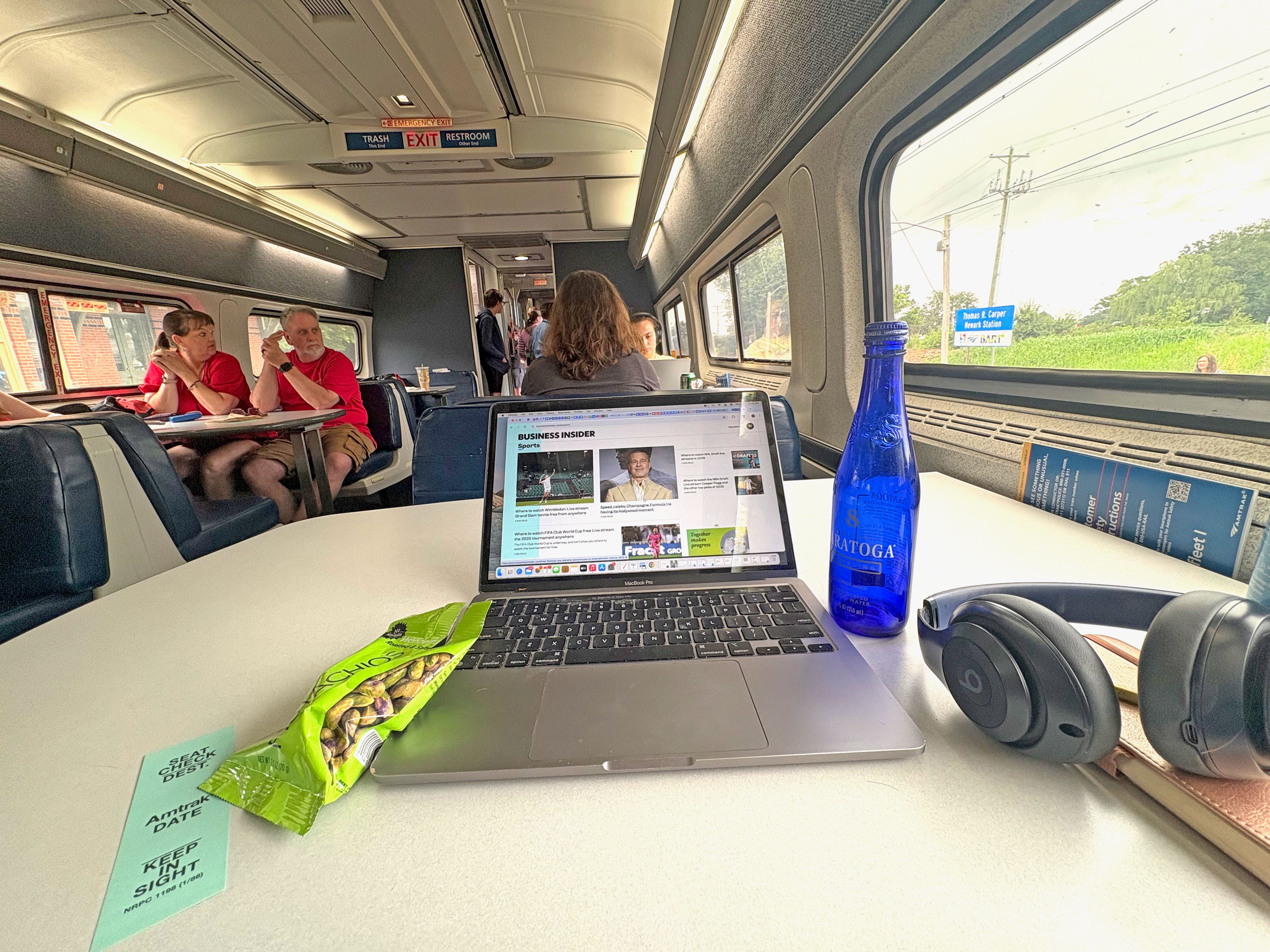 A laptop, bag of pistachios, bottle of water, and pair of headphones on a booth-style table on a train.