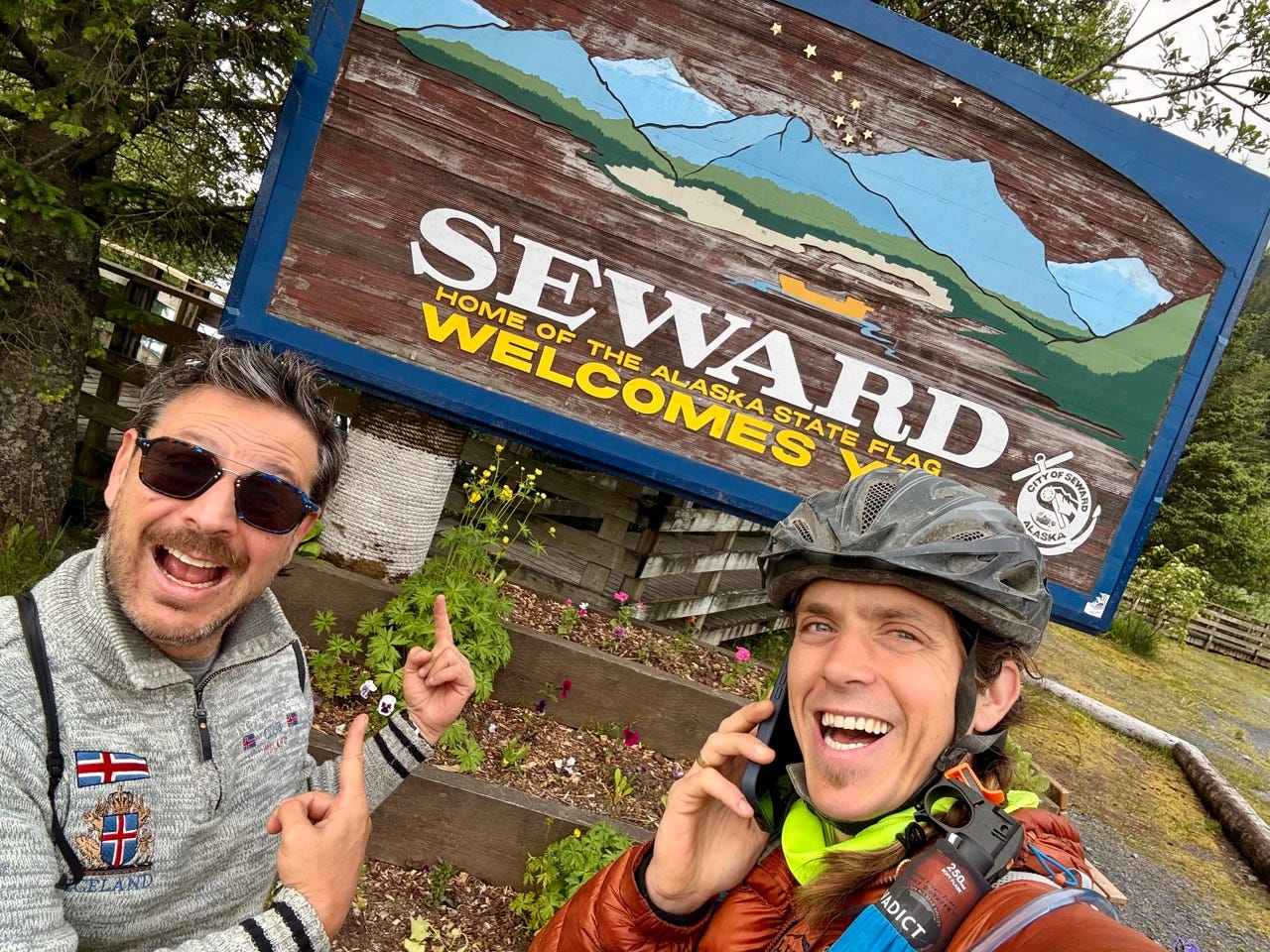 Author Ash Jurberg smiling with man in front of Seward welcomes you sign, smiling