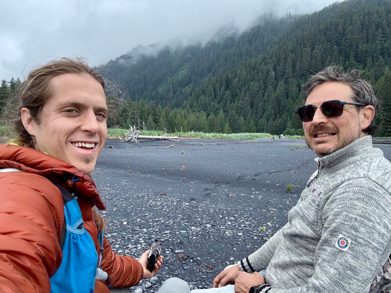 Two men smiling in front og trees, rocky field