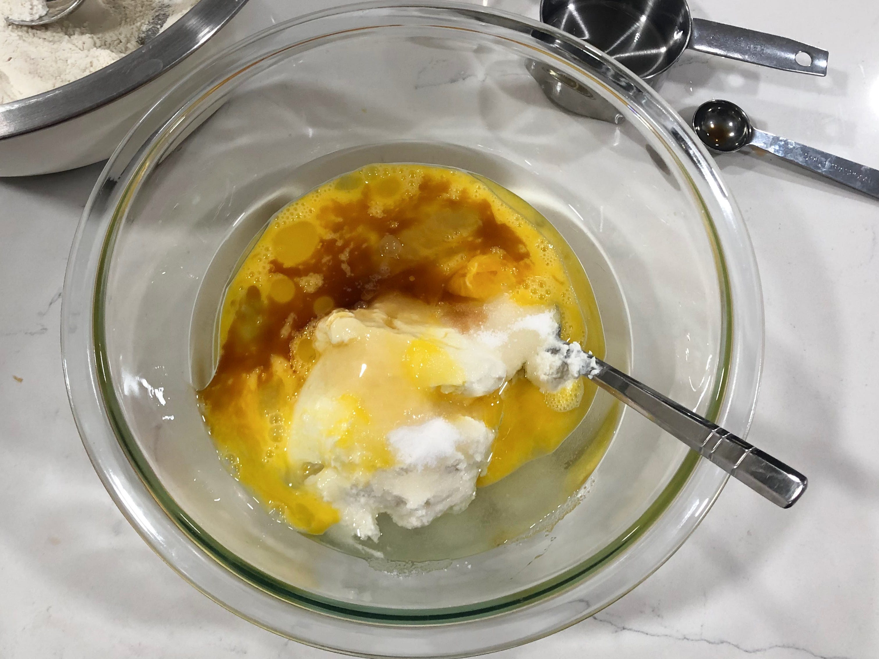 A mixture of ingredients, including eggs, in a clear bowl. There is also a spoon in the bowl.
