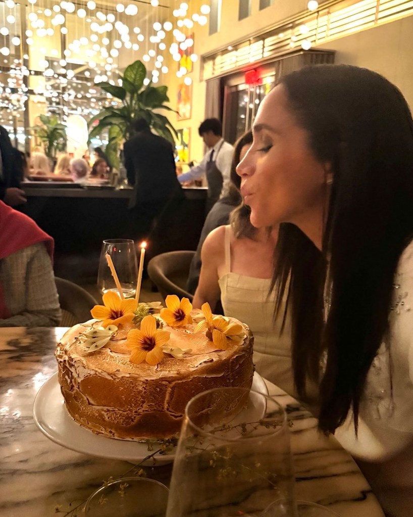 Meghan Markle blowing out a candle on a birthday cake decorated with yellow flowers.