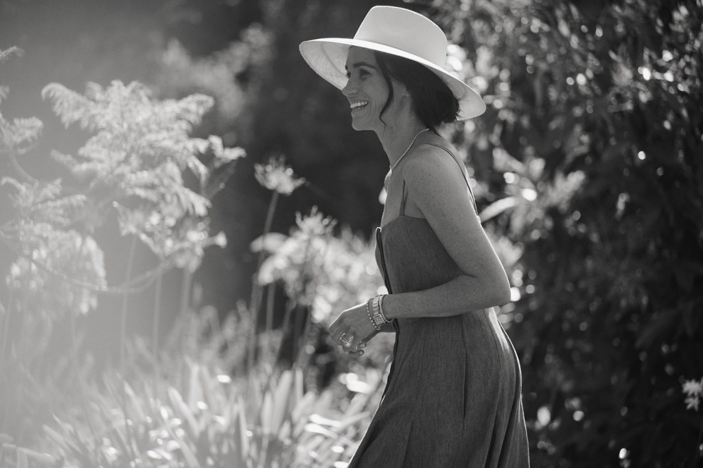 Meghan Markle smiling in a sun hat and dress.