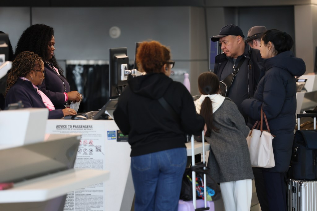 Man in purple jacket looking dejected while another man and baby stroller wait with luggage.