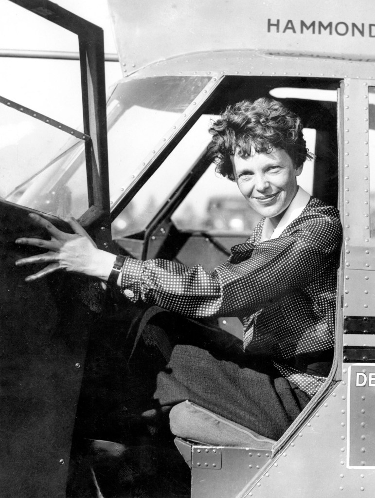 Amelia Earhart smiling from the cockpit of her plane.
