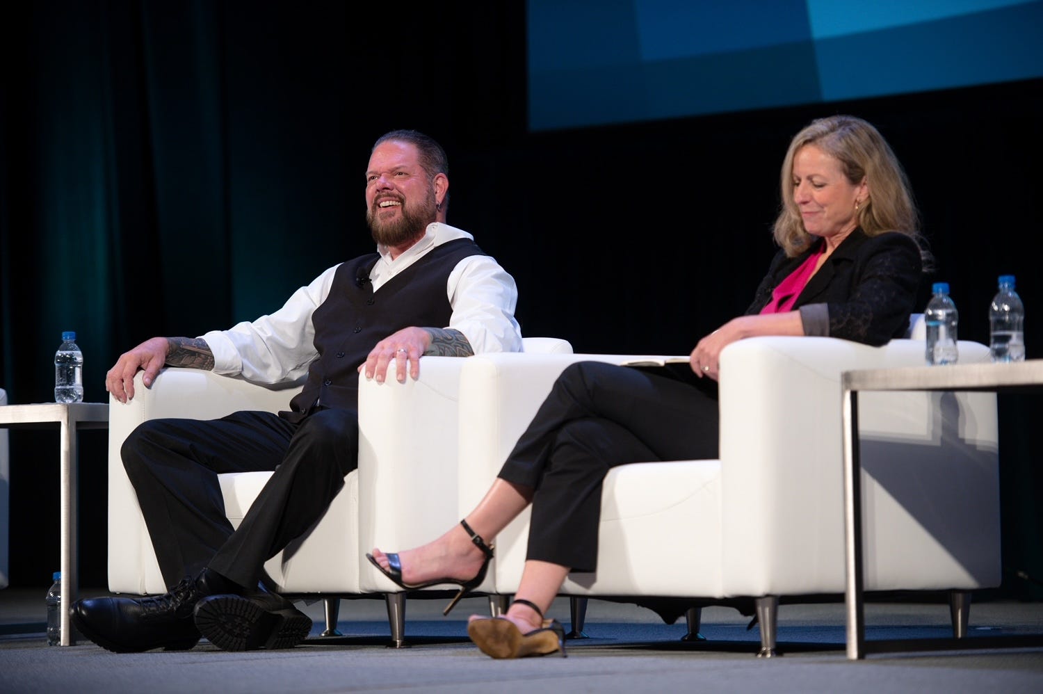 Scott payne in a black and white suit at a conference, sitting in a white chair