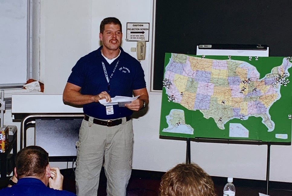 Young Scott Payne in blue shirt and tan pants standing at front of a classroom with a map of the US.