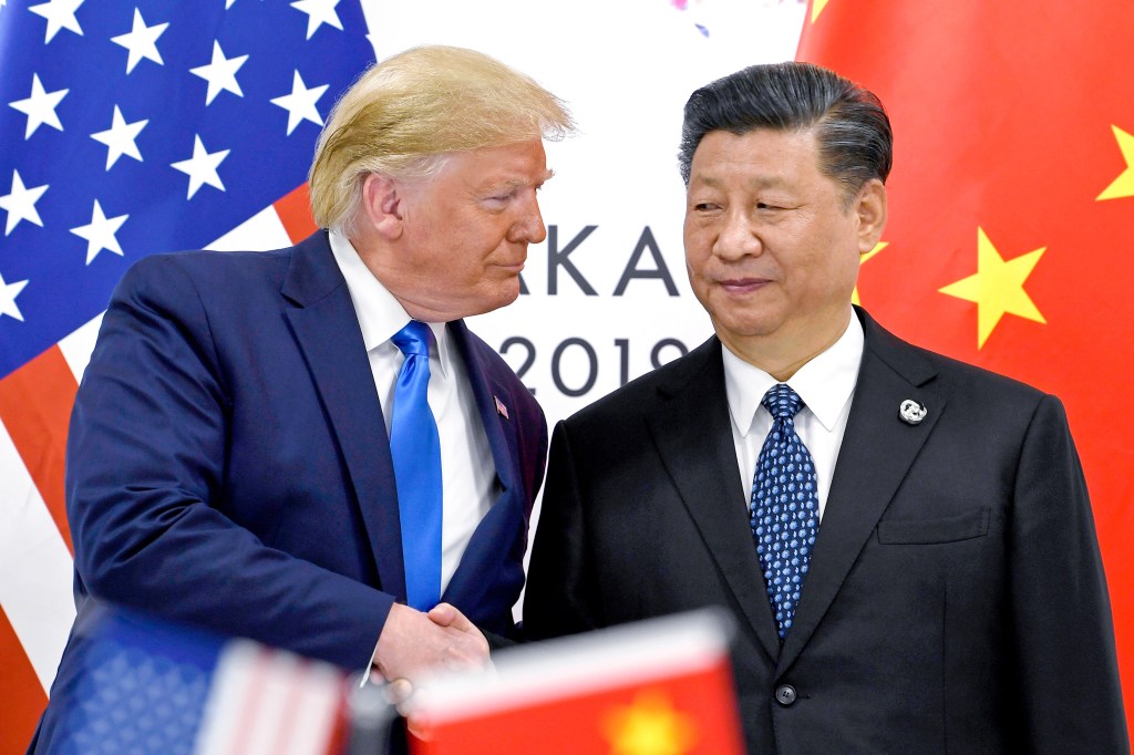Donald Trump and Xi Jinping shake hands in front of the US and Chinese flags.