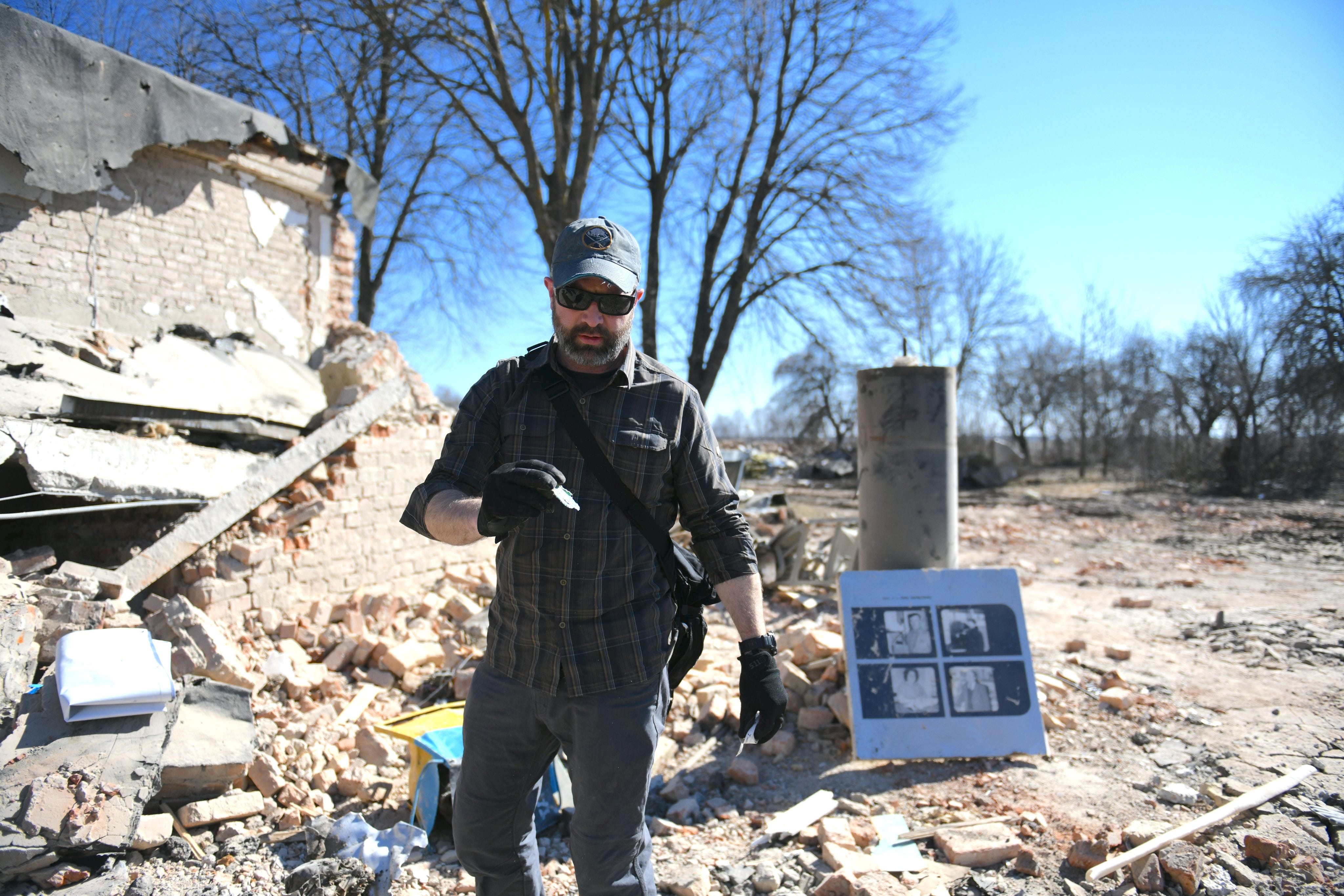 Brian Castner looking at remnants of an explosion with a demolished building in the background.