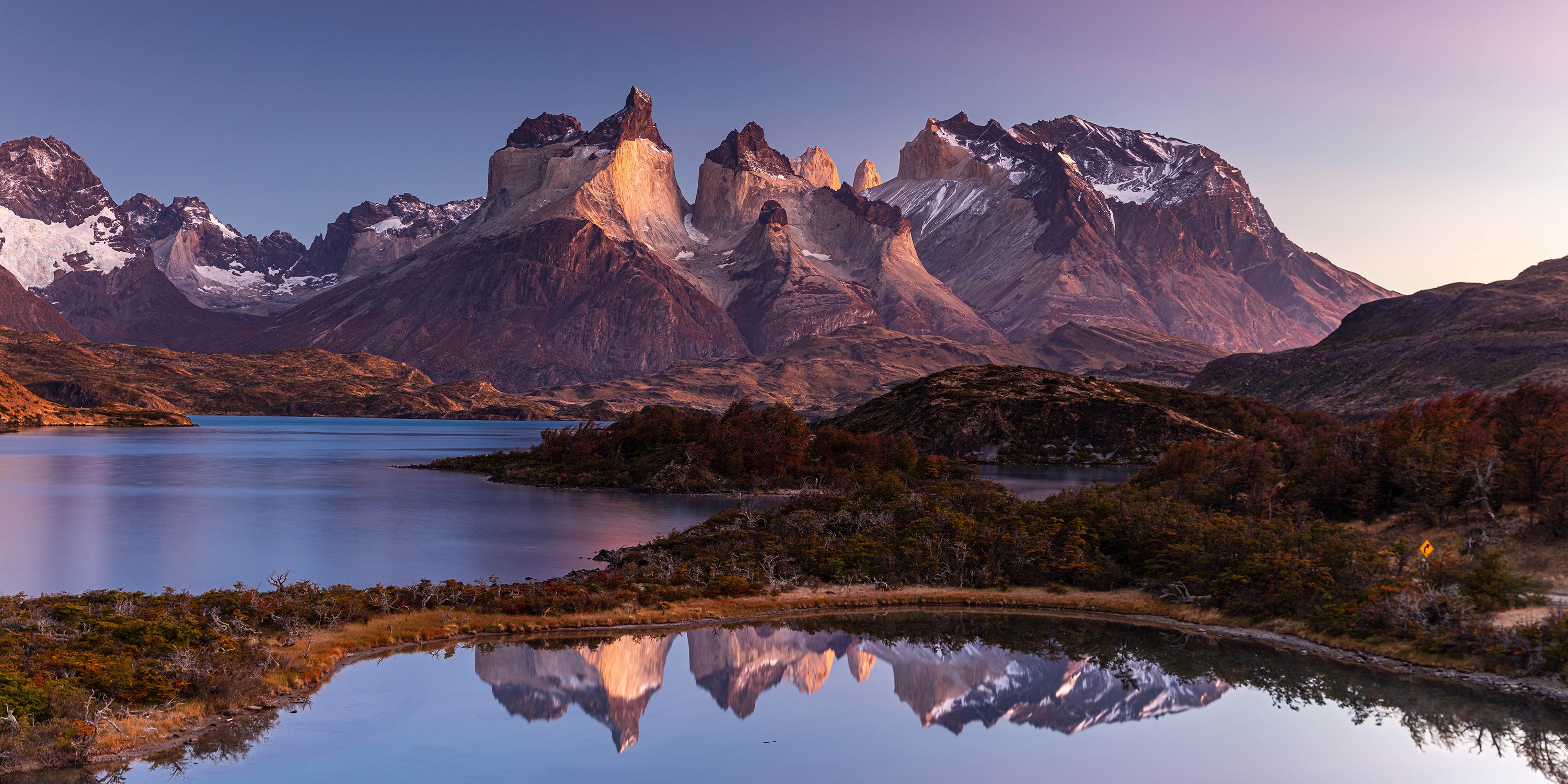 A panoramic view of a steep and rocky mountain range, seen beyond a lake.
